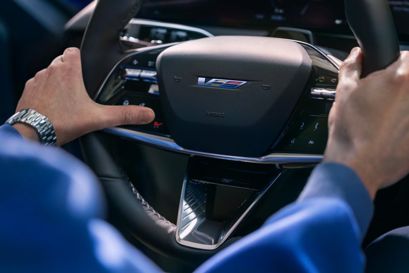 Close-up of a Man About to Press the V-Button on the 2026 OPTIQ-V Steering Wheel | Landmark Cadillac in Springfield IL